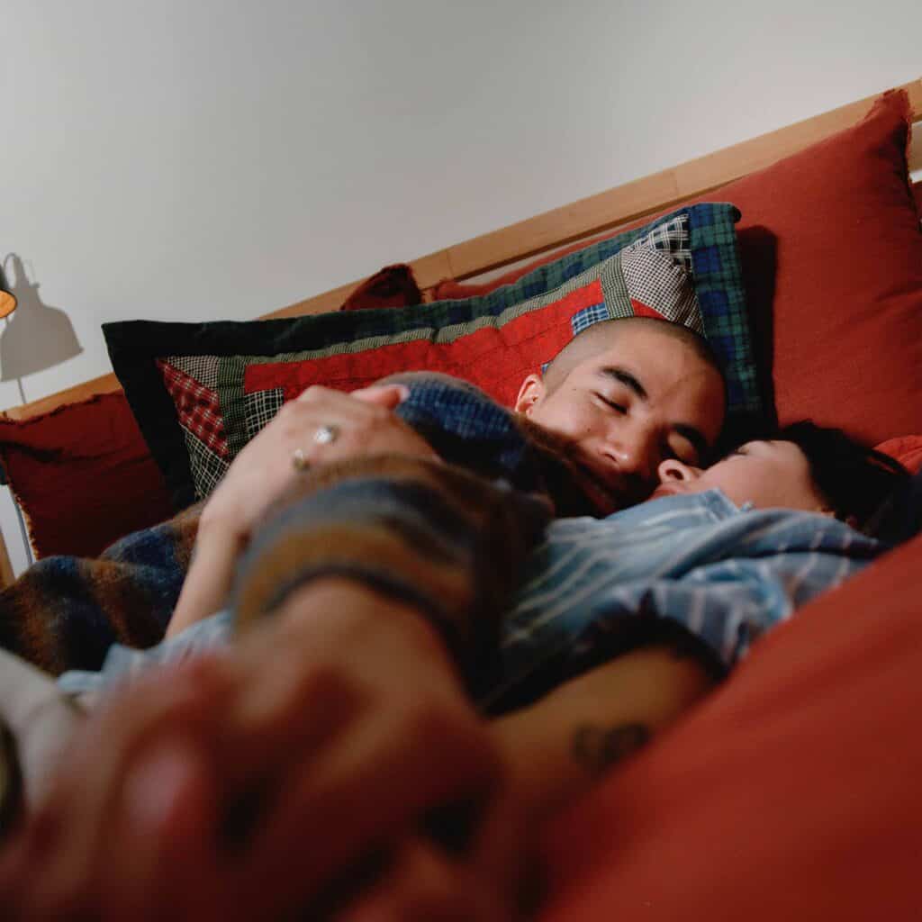 A married couple smiling and cuddling in bed.